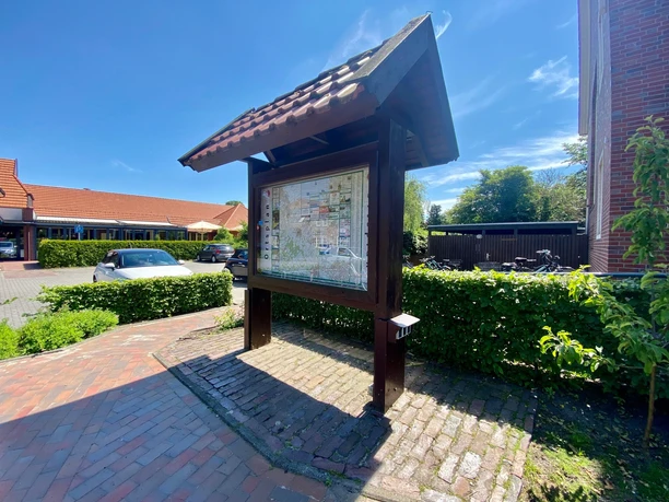 Ladestation E-Bike.jpg Karte mit Orten unter einem Dach aus Holz, im Sonnenlicht, auf Backsteinweg.