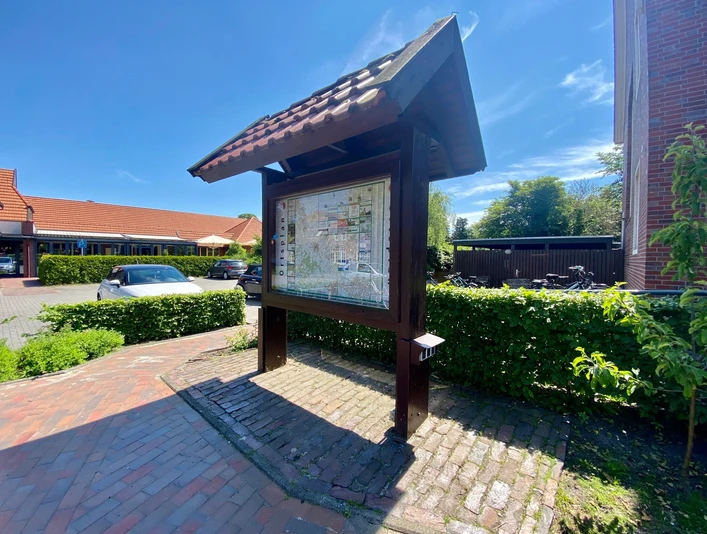 Ladestation E-Bike.jpg Karte mit Orten unter einem Dach aus Holz, im Sonnenlicht, auf Backsteinweg.