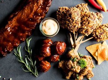 Grillerlebnis Verschiedene Grillgerichte auf einem Tisch: BBQ-Rippchen, Fleischspieße, Dip und Kräuter.