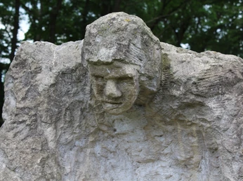 Steinerne Skulptur "Der Kärrner" mit ausdrucksstarkem Gesicht inmitten von Bäumen im Park Etelsen.