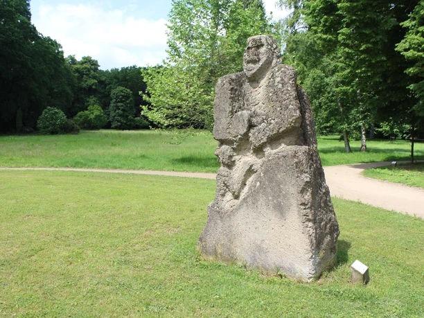 Steinskulptur mit grober Struktur im Park Etelsen, zeigt menschliche Figur mit Kopf und Rumpf.