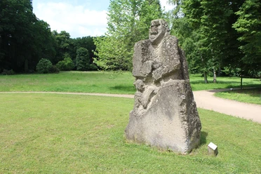 Skulptur im Park Etelsen"Kopfgeburt" Steinskulptur mit grober Struktur im Park Etelsen, zeigt menschliche Figur mit Kopf und Rumpf.