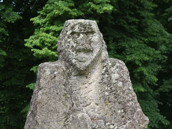 Steinskulptur "Kopfgeburt" im Park Etelsen, umgeben von dichtem grünen Blattwerk.