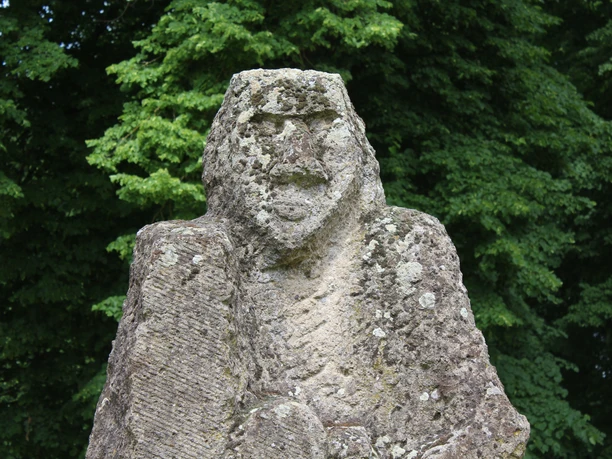 Skulptur im Park Etelsen"Kopfgeburt" Steinskulptur "Kopfgeburt" im Park Etelsen, umgeben von dichtem grünen Blattwerk.