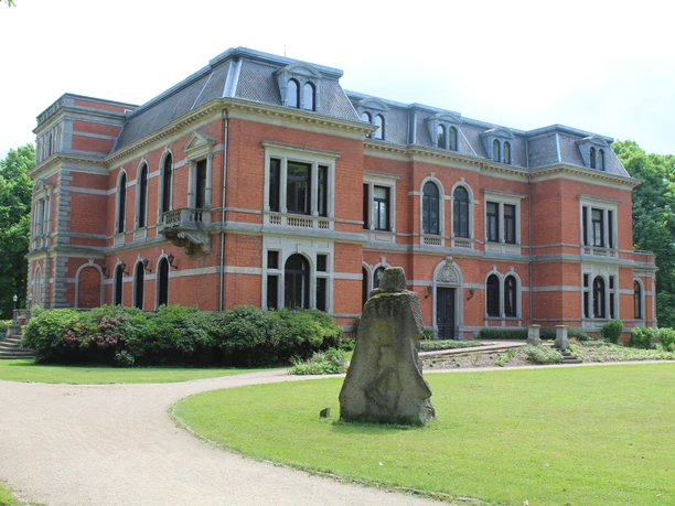 Schloss Etelsen erhebt sich majestätisch mit der Skulptur "Kopfgeburt" im gepflegten Parkgelände.