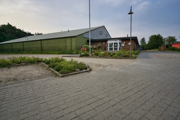 Tennishalle Große grüne Tennishalle mit Backstein-Eingangsbereich und gepflastertem Vorplatz.