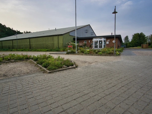Tennishalle Große grüne Tennishalle mit Backstein-Eingangsbereich und gepflastertem Vorplatz.