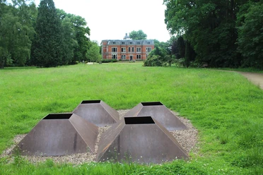Vier metallene pyramidale Strukturen auf Kiesfläche, umgeben von grüner Wiese, im Park von Schloss Etelsen.