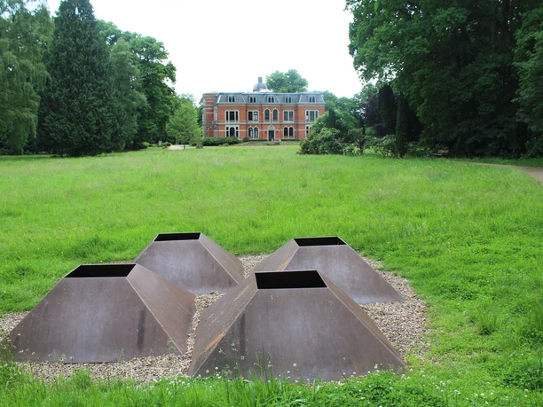 Skulpture im Park Etelsen "vier meere" Vier metallene pyramidale Strukturen auf Kiesfläche, umgeben von grüner Wiese, im Park von Schloss Etelsen.
