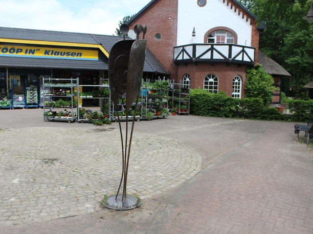 Eine filigrane Metallskulptur steht vor einem Geschäft in Martfeld, umgeben von Pflanzen.