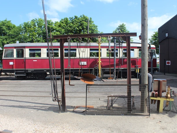 Museums-Eisenbahn Bruchhausen-Vilsen Roter Oldtimer-Zugwagen und Eisenbahnausrüstung auf einem sonnigen Bahngelände mit grünen Bäumen.