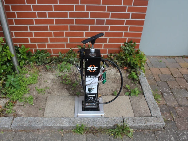 Lufttankstelle Asendorf Fahrradluftpumpstation vor rotem Ziegelgebäude auf Steinplatte, mit Schläuchen und Manometer ausgestattet.