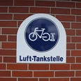 Lufttankstelle für Fahrräder mit dunkelblauem Schild auf rotem Backstein in Asendorf.