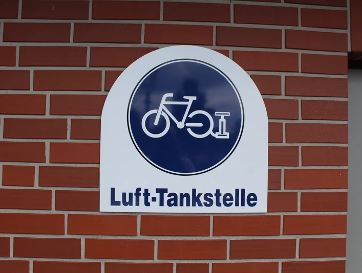 Lufttankstelle für Fahrräder mit dunkelblauem Schild auf rotem Backstein in Asendorf.