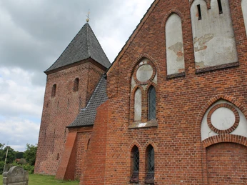 Kirche Daverden Backsteinkirche aus dem Mittelalter mit markantem Glockenturm und Spitzdach unter wolkigem Himmel.