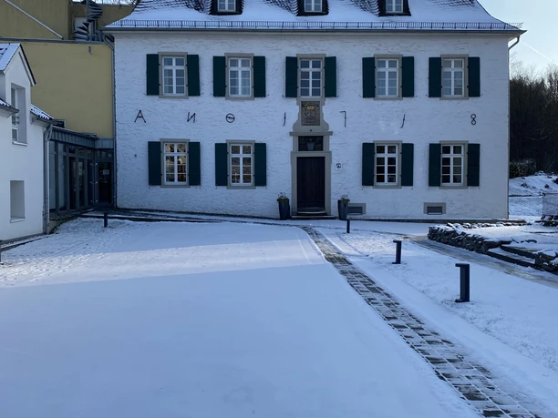 Haus Landscheid <p>Historisches Gebäude im Winter, mit schneebedecktem Hof und blauen Fensterläden.</p>