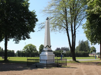 Denkmal Marktplatz Bruchhausen-Vilsen Ein weißer Obelisk mit Skulptur auf grünem Platz, umgeben von Bäumen, in Bruchhausen-Vilsen.