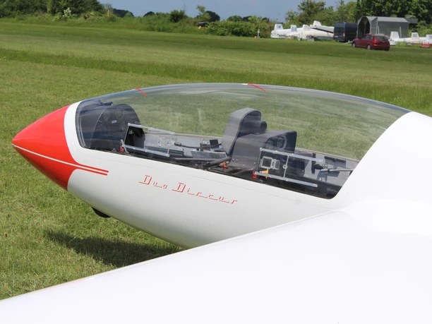 A white glider, marked in red, stands on a green meadow, ready to take off.