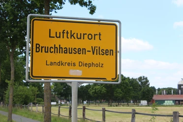 Plaatsnaambord voor het luchtkuuroord Bruchhausen-Vilsen in het district Diepholz, omgeven door groene bomen.