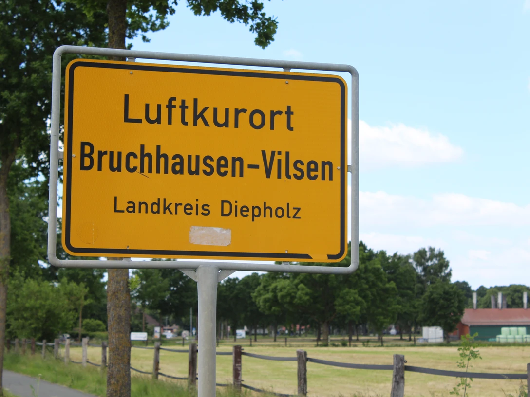 Ortsschild Ortsschild für den Luftkurort Bruchhausen-Vilsen im Landkreis Diepholz, umgeben von grünen Bäumen.Town sign for the climatic health resort of Bruchhausen-Vilsen in the district of Diepholz, surrounded by green trees.Byskilt for det klimatiske kursted Bruchhausen-Vilsen i distriktet Diepholz, omgivet af grønne træer.Plaatsnaambord voor het luchtkuuroord Bruchhausen-Vilsen in het district Diepholz, omgeven door groene bomen.