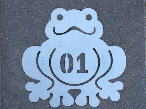 Poggenpad.jpg Metallplakette mit lachendem Froschmotiv und der Nummer 01 auf grauem Hintergrund.