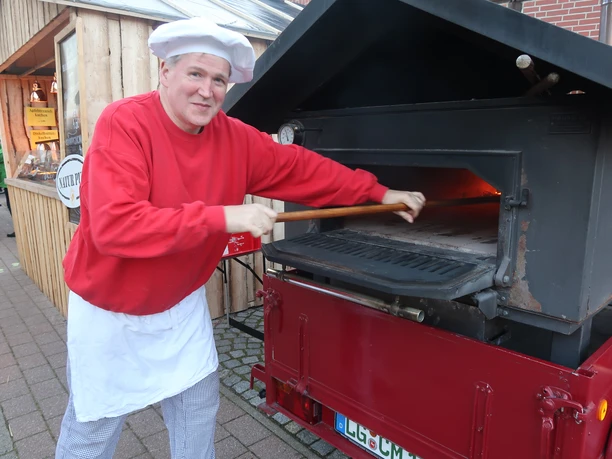 Bäcker Müller Bäckermeister Christian Müller schiebt Brot in einen mobilen Holzbackofen auf einem Anhänger.