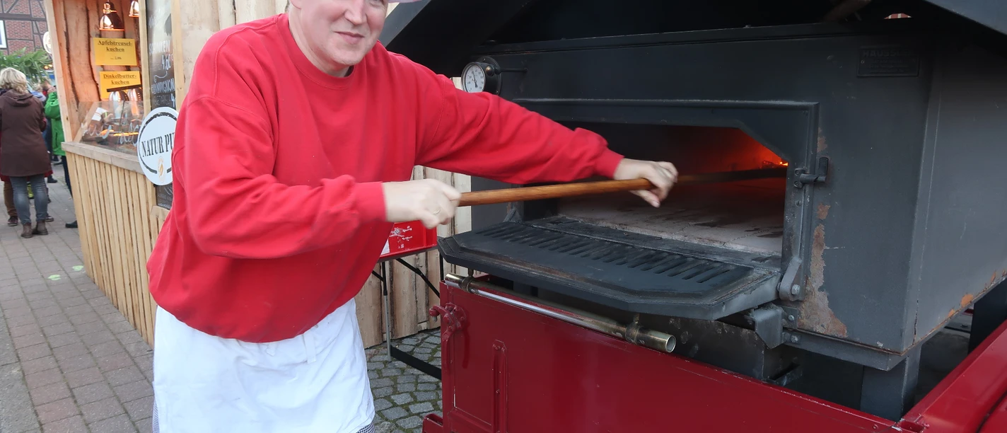 Bäcker Müller Bäckermeister Christian Müller schiebt Brot in einen mobilen Holzbackofen auf einem Anhänger.