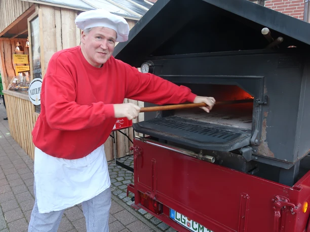Bäcker Müller Bäckermeister Christian Müller schiebt Brot in einen mobilen Holzbackofen auf einem Anhänger.