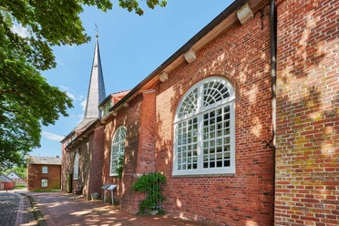 Beeindruckende rote Backsteinkirche in Oberndorf mit spitzem Turm und hellen Bogenfenstern.