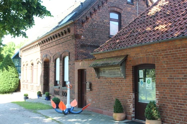 Traditionelles Klinkergebäude mit Anker als Dekoration vor der Tür, umgeben von grünen Sträuchern.