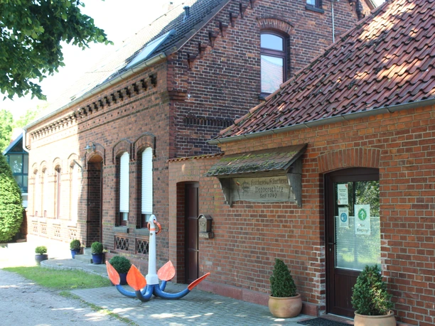 Dobberschütz Nienburg Traditionelles Klinkergebäude mit Anker als Dekoration vor der Tür, umgeben von grünen Sträuchern.