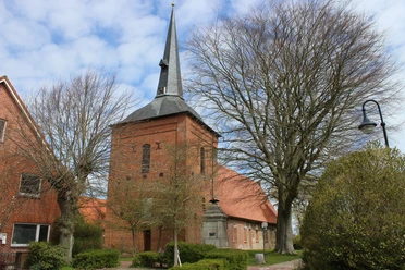 Markante St. Vitus Backsteinkirche in Belum mit hohem, dunklem Spitzturm unter blauem Himmel.