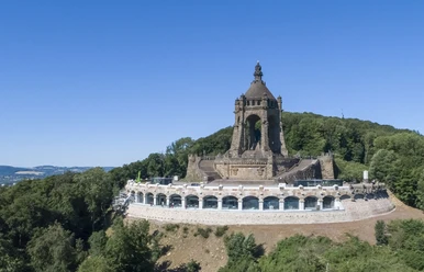 Kaiser-Wilhelm-Denkmal Kaiser-Wilhelm-Denkmal auf Hügel, umgeben von Wald, mit Aussicht auf Landschaft unter blauem Himmel.