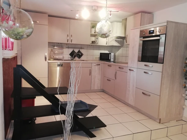 Moderne Einbauküche mit weißen Fronten, Elektrogeräten und beleuchtetem Deckenbereich auf hellen Fliesen.