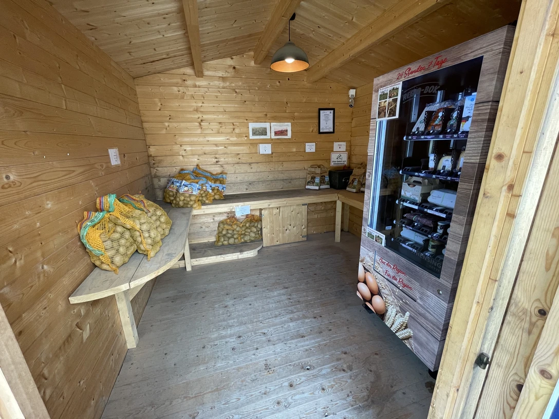 Hofladen von Albert Heeren Kleiner Holzraum mit Verkaufsautomat und Säcken frischer Kartoffeln auf Holzbänken.