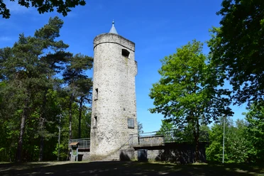 Aussichtsturm Derschlag Alter steinerner Aussichtsturm im Wald bei sonnigem Wetter, umgeben von grünen Bäumen und blauem Himmel.