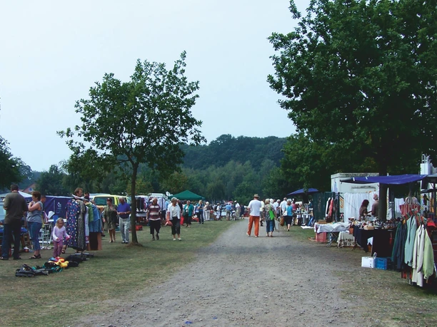 Mardorf Trödelmarkt Der Trödelmarkt in Mardorf zeigt Händler und Besucher entlang eines Schotterwegs mit bunten Ständen.