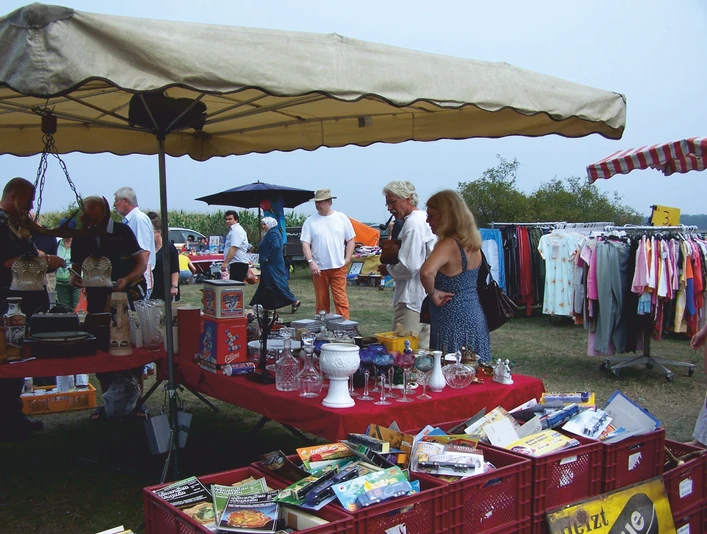 Mardorf Trödelmarkt Ein Flohmarkt in Mardorf mit Menschen, die an Ständen mit Glaswaren und Kleidung stöbern.