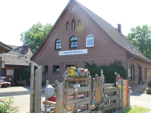 Haus der Vielfalt Backsteingebäude mit Satteldach und Schriftzug "Haus der Vielfalt", umgeben von Bäumen und Holzzaun.