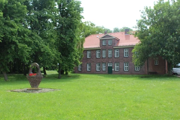 Altes Amtsgericht Historisches Backsteingebäude mit rotem Dach, umgeben von grüner Rasenfläche und schattenspendenden Bäumen.