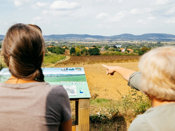 Blick ins Weserbergland Zwei Personen betrachten von einem Aussichtspunkt aus eine weite Landschaft mit hügeliger Ferne.