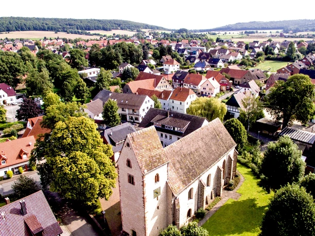 Blick auf Langenholzhausen Langenholzhausen mit grünem Hügelpanorama, Kirche im Zentrum, umgeben von Wohnhäusern und Bäumen.
