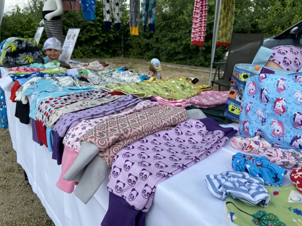 IMG_1605.JPG Ein Markttisch bietet bunte Kinderkleidung mit fröhlichen Mustern und Farben zur Auswahl an.