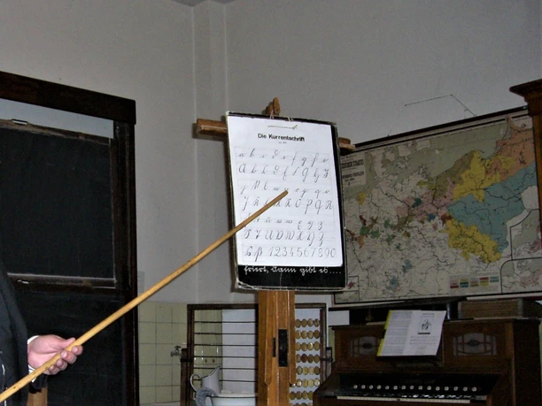 Schulmuseum Katterbach Eine historische Schulklasse mit Karte, Tafel und Schönschriftübungen, Position auf eine Schreibtafel gerichtet.