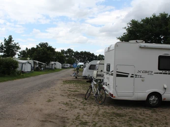 Wohnmobilstellplatz Marina Mehlbergen Wohnmobile stehen geparkt auf einem ruhigen Kiesplatz, umgeben von Bäumen unter einem klaren Himmel.