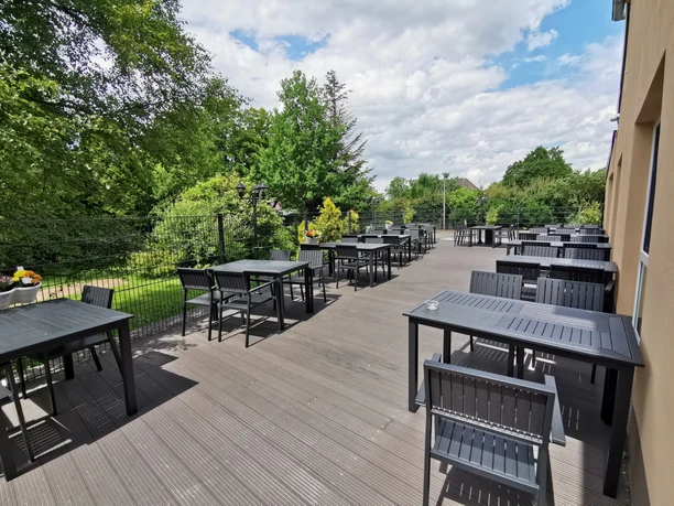 Asia-Restaurant Fang Leere Außenterrasse eines Asia-Restaurants mit schwarzen Tischen und Stühlen, umgeben von grünen Bäumen und Sträuchern