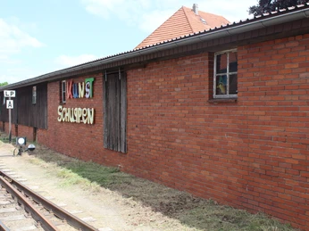 Kunstschuppen Asendorf Backsteingebäude mit grafischem Schriftzug "Kunstschuppen" und Schienen sowie Signal im Vordergrund.