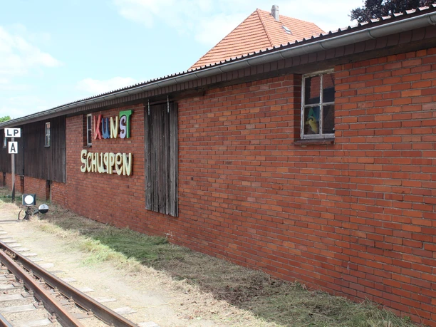 Kunstschuppen Asendorf Backsteingebäude mit grafischem Schriftzug "Kunstschuppen" und Schienen sowie Signal im Vordergrund.