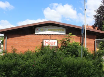 Kunstschuppen Asendorf Roter Backsteinbau des Kunstschuppens in Asendorf, umrahmt von grüner Vegetation unter blauem Himmel.