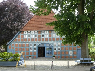 Historisches Fachwerkhaus mit blauen Fensterläden und rotem Ziegeldach unter grünen Bäumen.